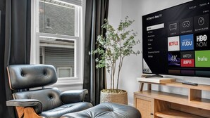 Una sala de estar moderna con un sofá de cuero, una mesa de centro de madera y un televisor de pantalla plana grande que muestra la interfaz de una plataforma de streaming.