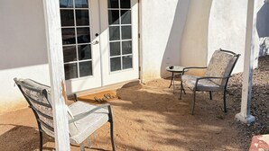 A covered patio area with two chairs, a small table, and a door with glass panels. - Large, well equipped Studio with Queen Bed and new bathroom. (Tucson)