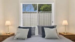 Ein Schlafzimmer mit einem Bett, zwei Nachttischen und einem Fenster mit Jalousien.