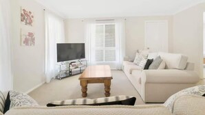 Ein Wohnzimmer mit Fernseher, Sofa, Couchtisch und einem Fenster mit Jalousien.