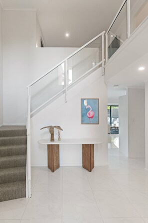 Eine moderne Treppe mit Glastrennwand, ein Holzkonsolentisch mit Dekoration und ein gerahmtes Kunstwerk an der Wand.