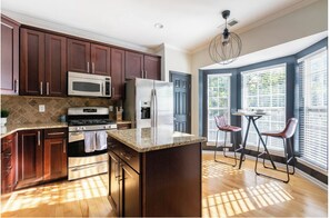 A modern kitchen with dark wood cabinets, stainless steel appliances, and a large island. - The Brix on Penn of Charlotte, Designer Townhome (Charlotte)