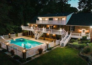 Uma casa de dois andares com piscina, várias varandas e área externa bem iluminada.