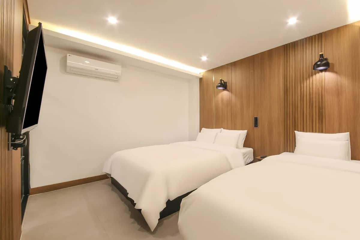 A hotel room with two beds, a TV, and a wooden accent wall.
