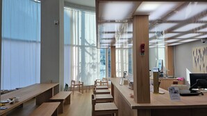 Un espacio de oficina moderno con escritorios y bancos de madera, ventanas amplias con cortinas translúcidas y una cámara de seguridad visible.