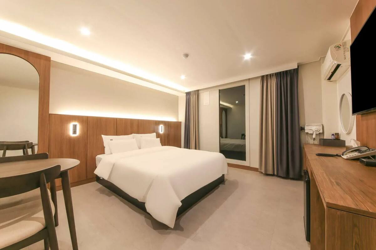 A hotel room with a bed, a desk, a chair, a TV, a mirror, and a sliding door.