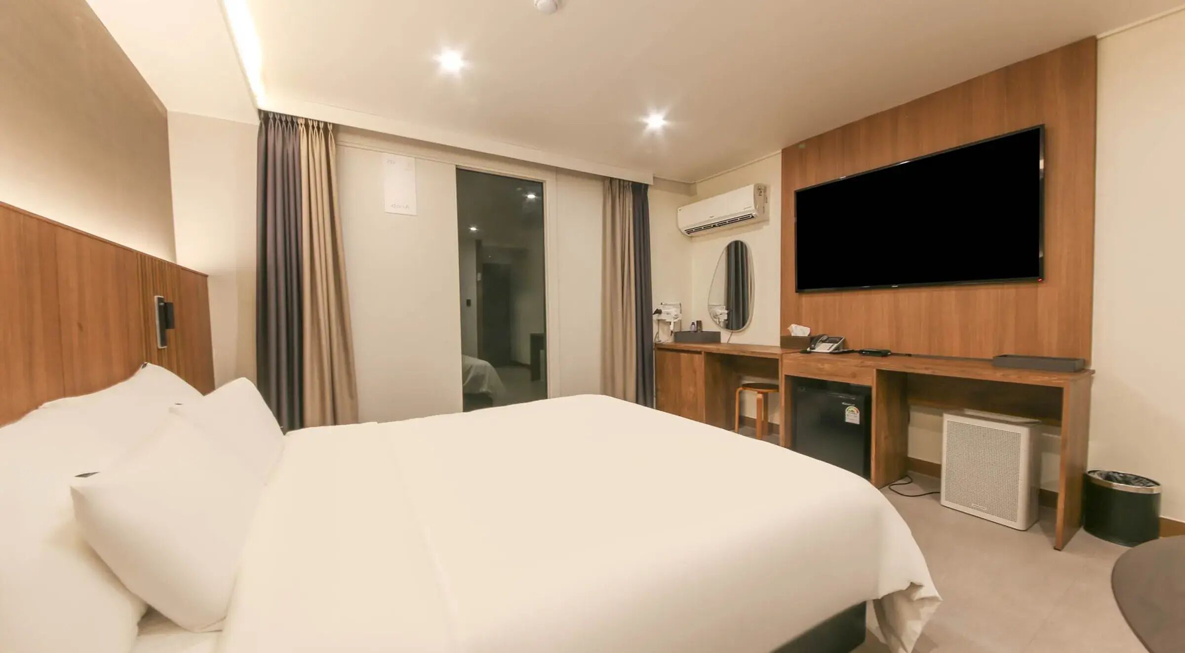 A hotel room with a bed, a desk, a television, and an air conditioning unit.