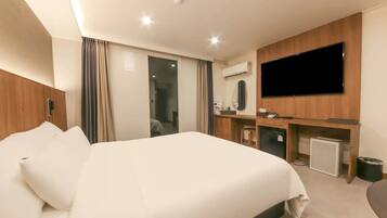 A hotel room with a bed, a desk, a television, and an air conditioning unit.