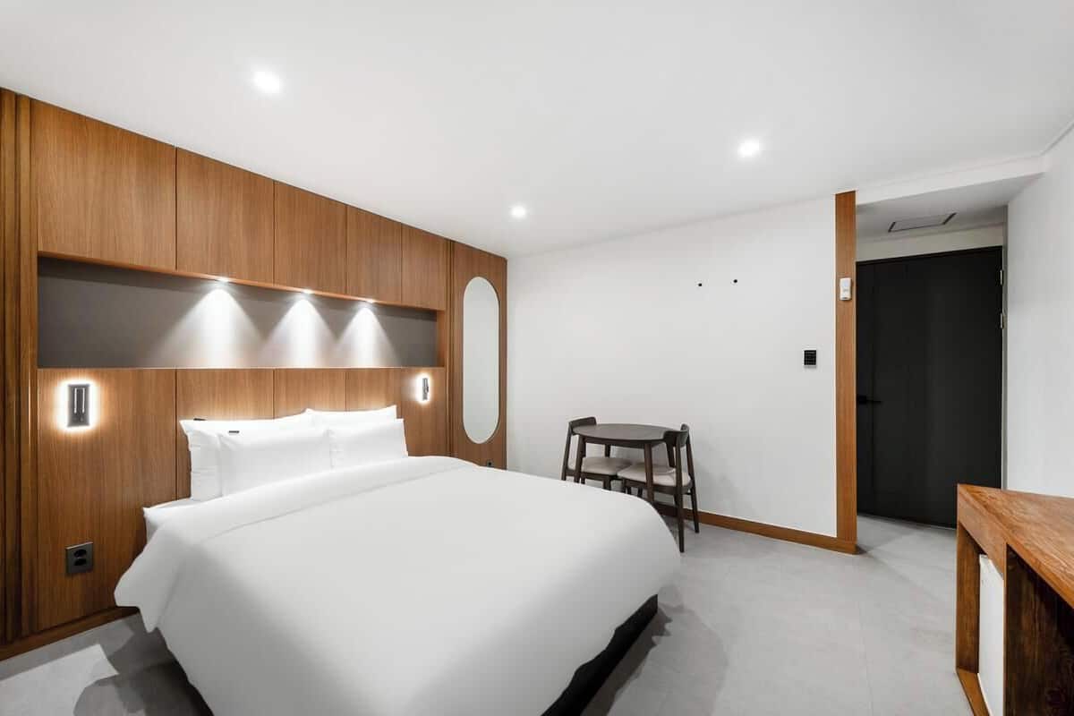 A modern hotel room with a large bed, a wooden headboard, a small table, and a chair.