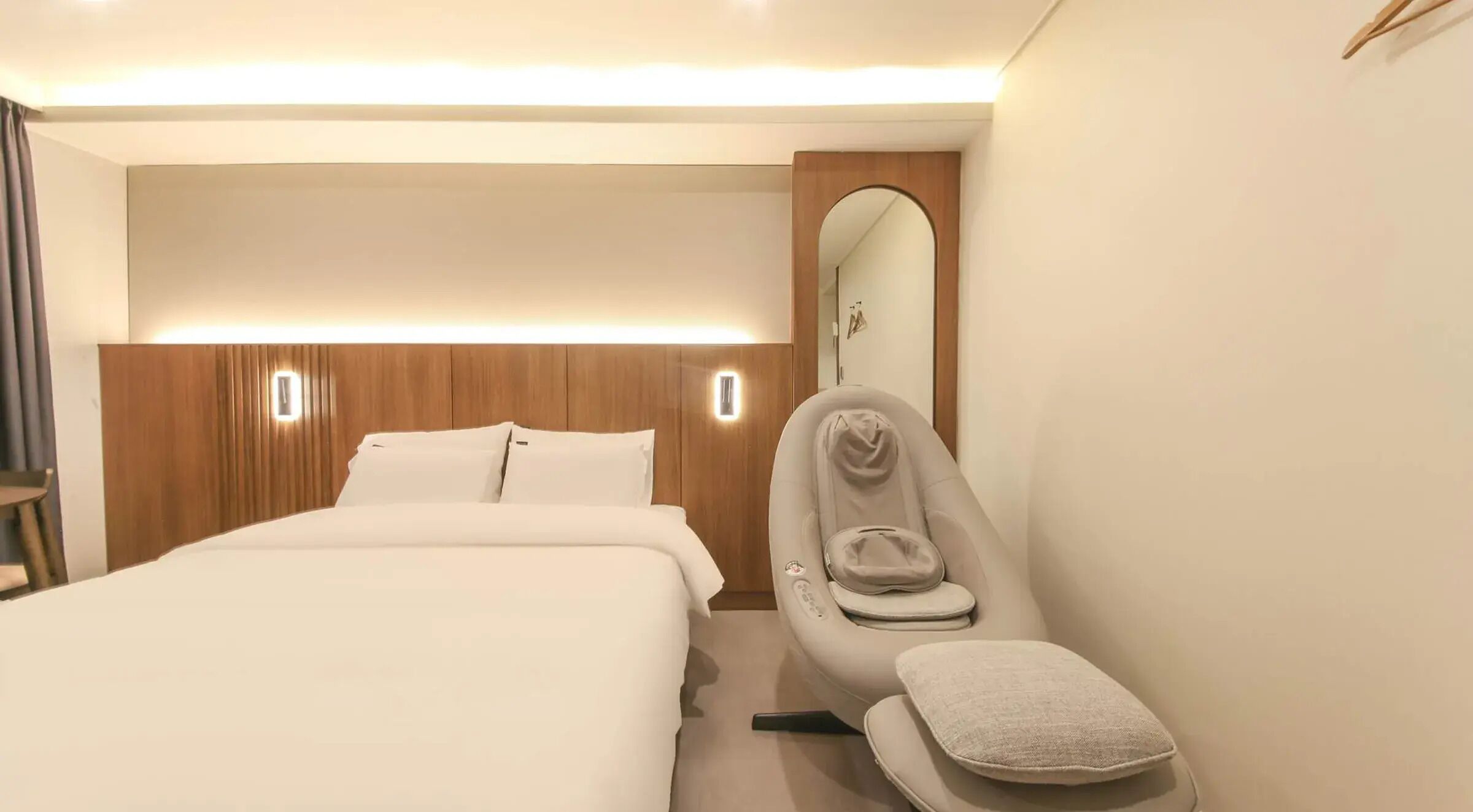 Une chambre d’hôtel avec un lit, un fauteuil de massage et un miroir.