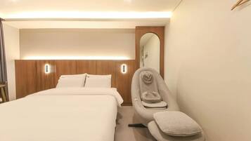Une chambre d’hôtel avec un lit, un fauteuil de massage et un miroir.