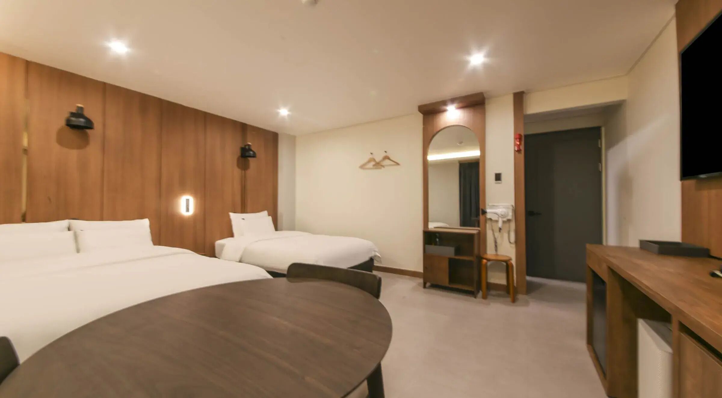 A hotel room with two beds, a round dining table, a mirror, and a TV.