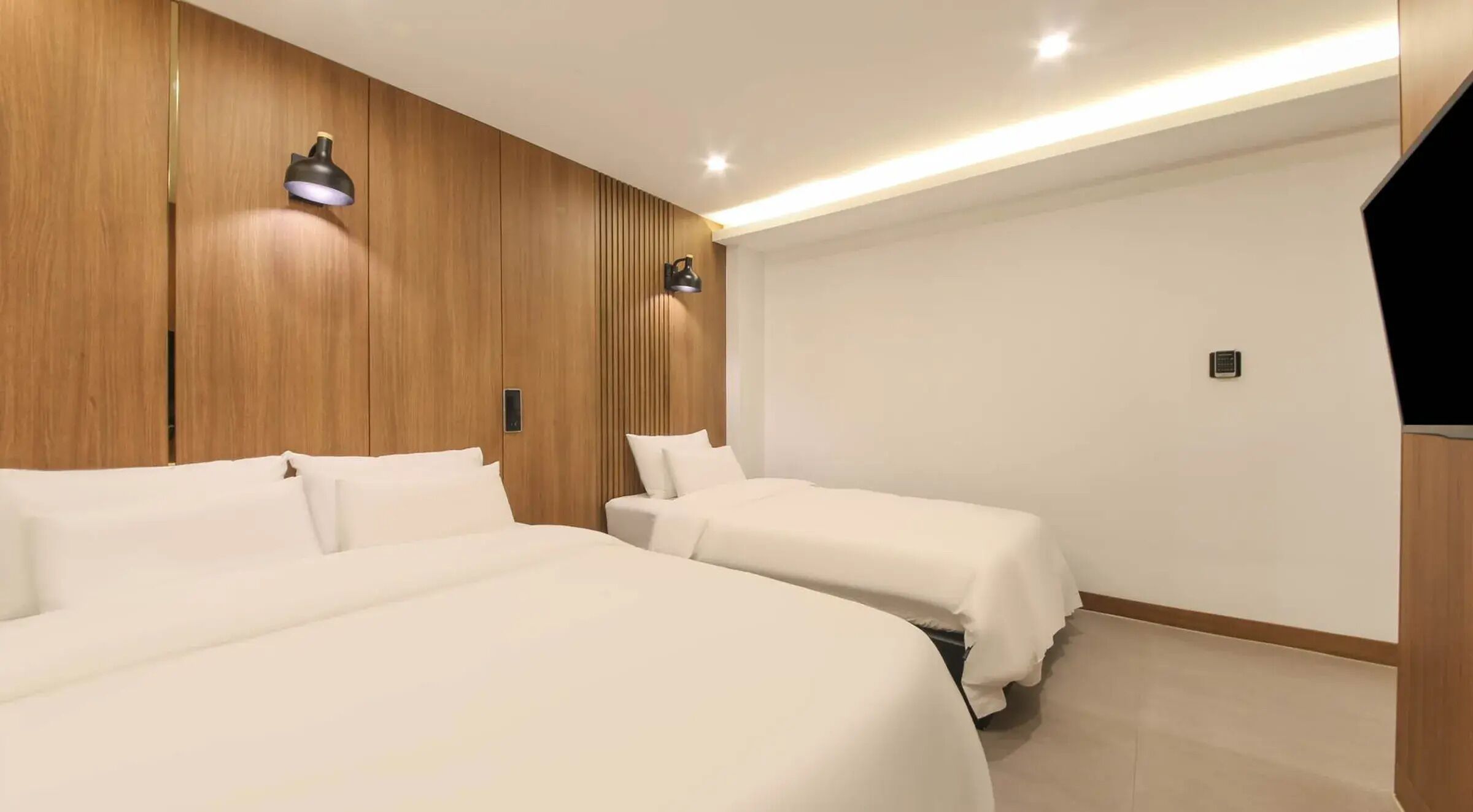 Habitación de hotel con dos camas, paneles de madera, una lámpara de pared y una luz en el techo.