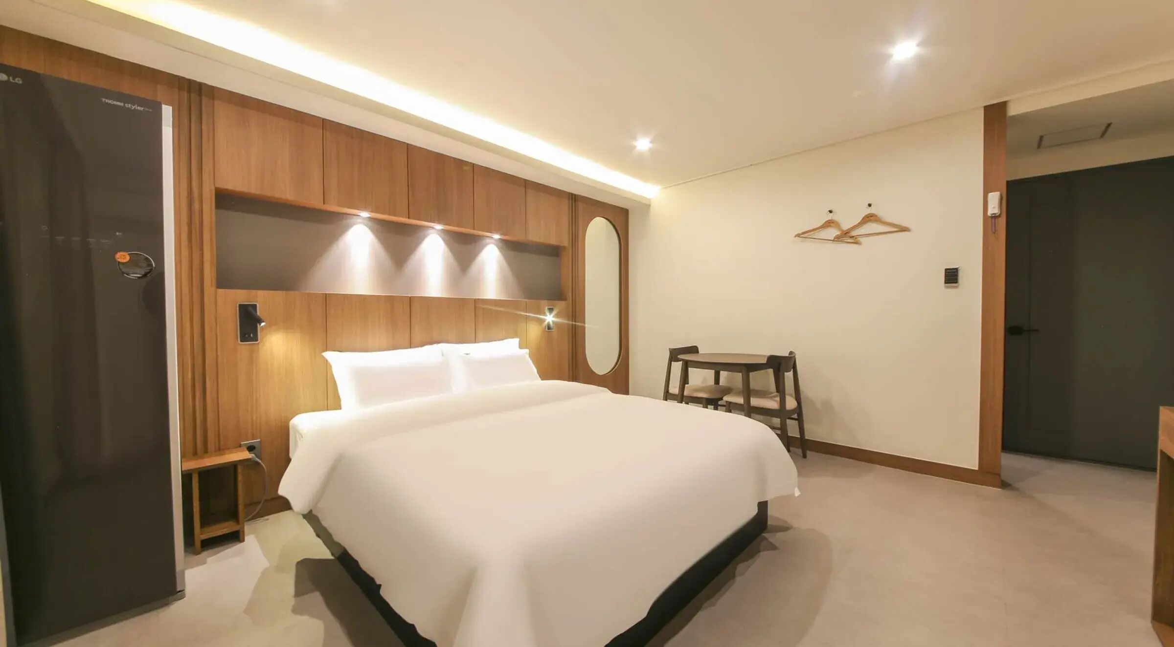 A hotel room with a large bed, a wooden wardrobe, a small table with chairs, and a mirror on the wall.