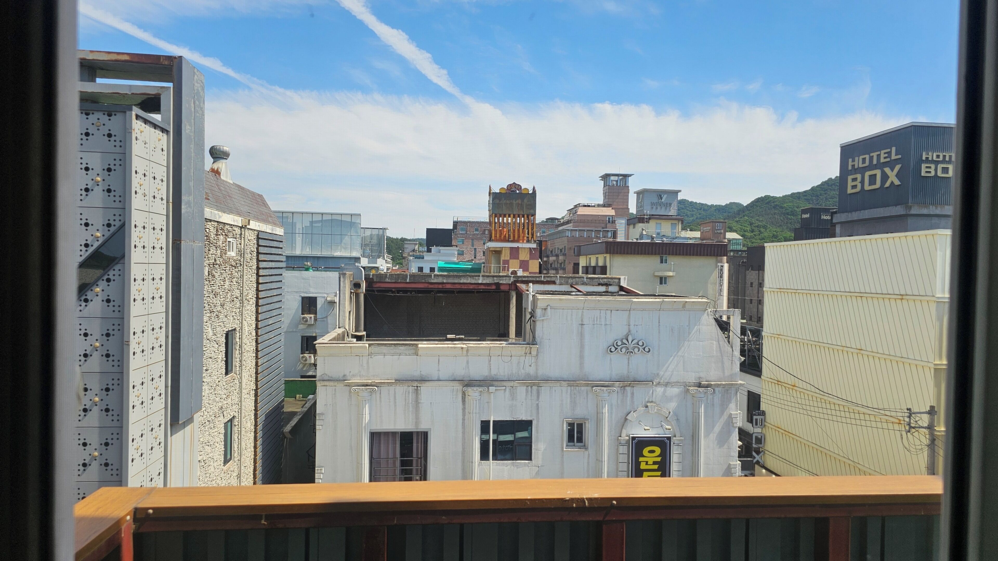 A cityscape with a prominent hotel box building, a traditional building with a tower, and a modern building with a metal facade.