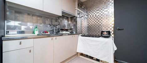 Una cocina compacta con armarios de tonos claros, encimera de acero inoxidable y salpicadero con estampado de cuadros.