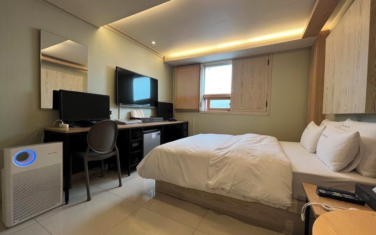 Una habitación de hotel con una cama, un escritorio con computadora, un televisor y una ventana.
