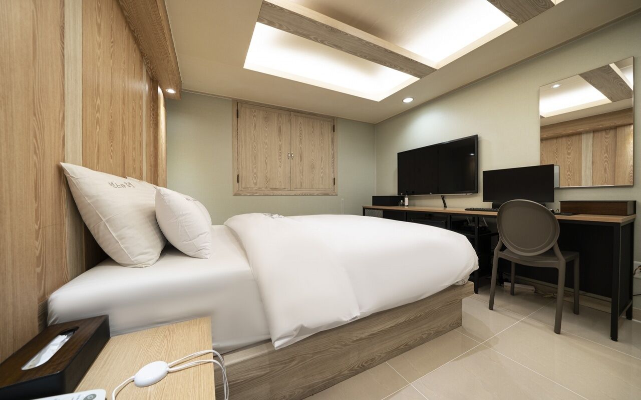 A modern bedroom with a bed, a desk, a chair, a television, and a large mirror.