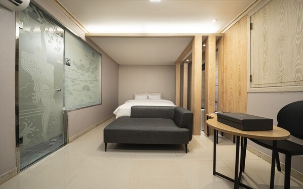 A compact hotel room with a bed, a sofa, a small table, and a glass partition with artwork. - Suwon Haenggung-dong Sunstar (Suwon)
