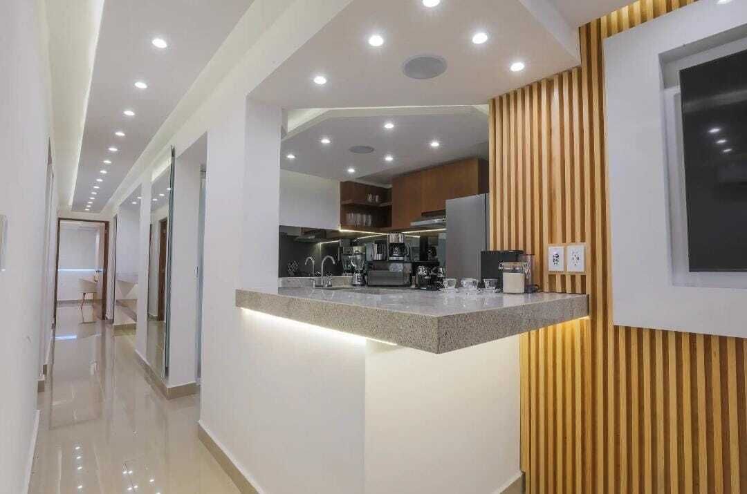 A modern kitchen with a granite countertop, stainless steel appliances, and recessed ceiling lighting.