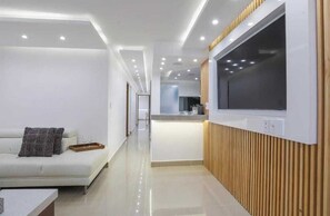 Ein modernes Hotelzimmer mit einem weißen Sofa, einer Wand als Holzdekor und einem großen, an der Wand montierten Fernseher.