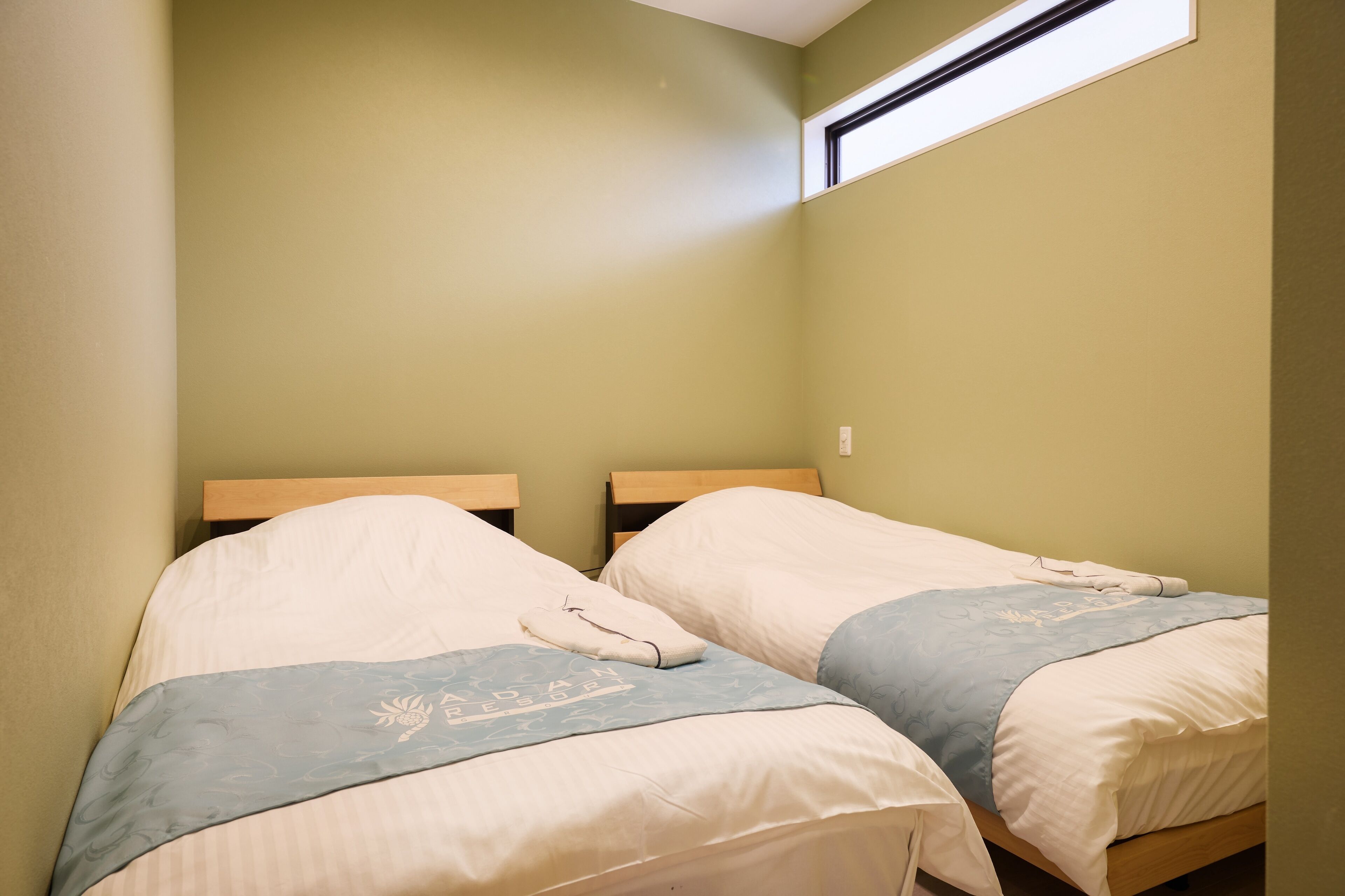Twee eenpersoonsbedden met houten hoofdeinden in een kamer met groene wanden en een dakraam.