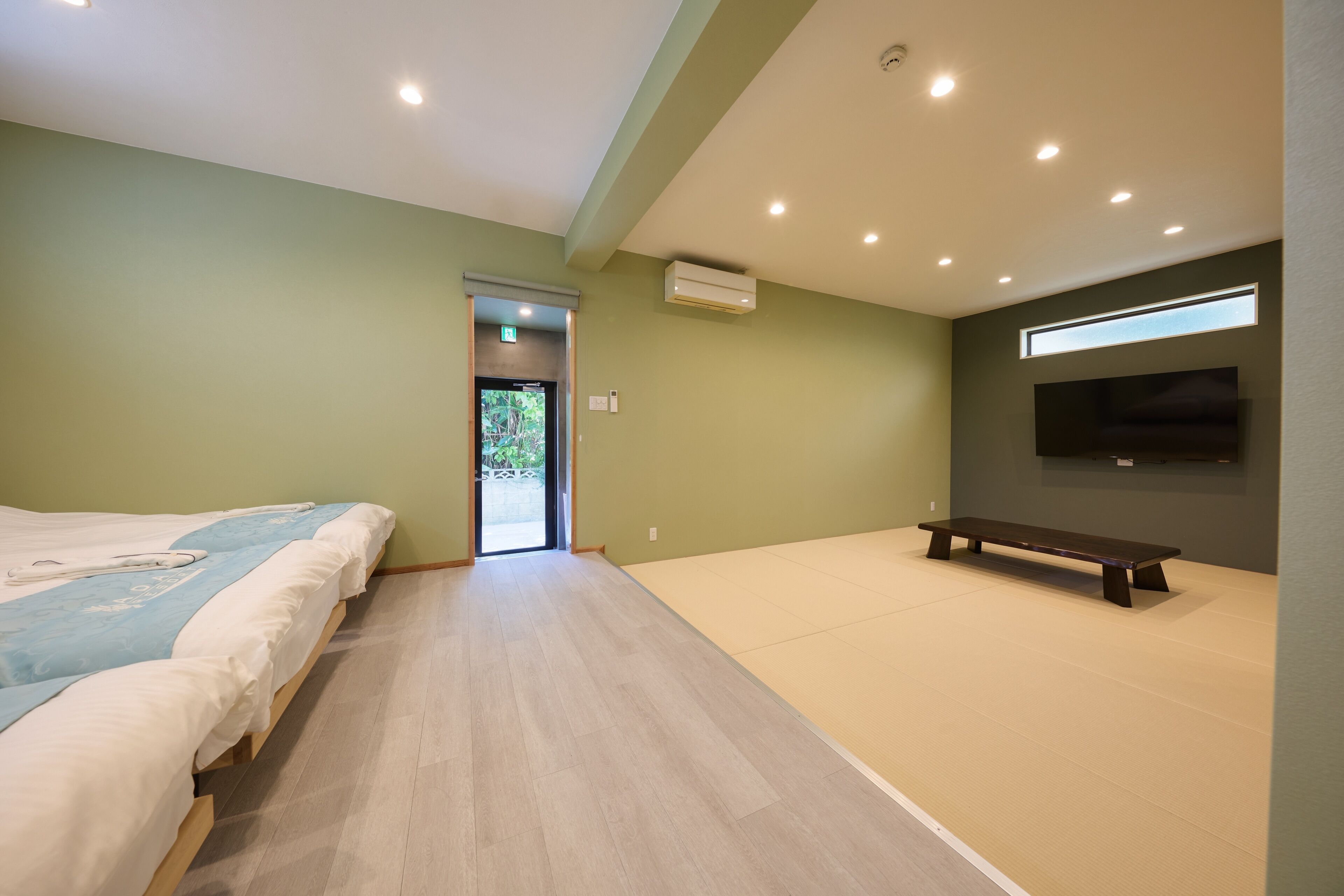 Quarto de hotel moderno com cama grande, um banco, TV de tela plana e uma janela ampla.