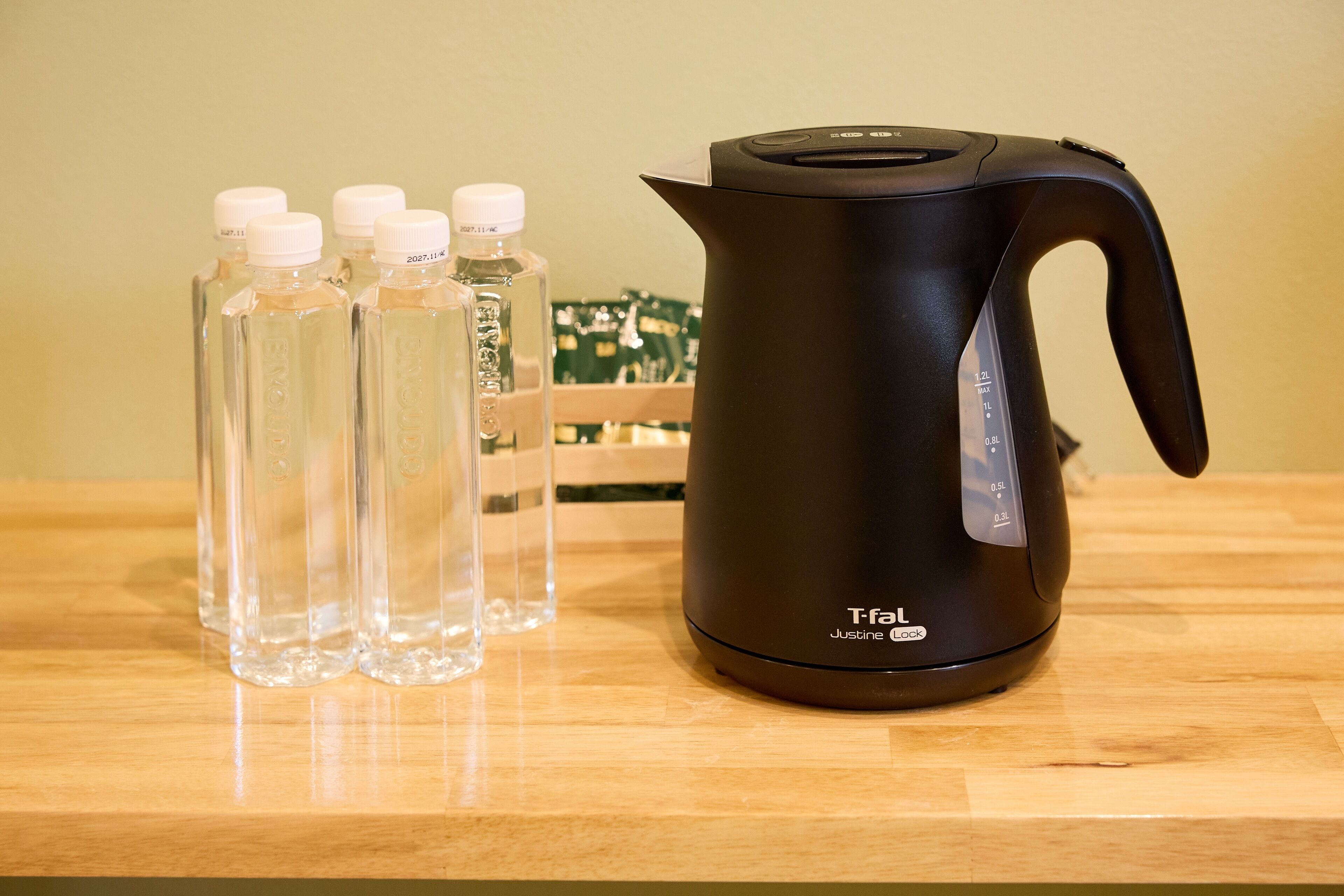 Een zwarte T-fal Justine waterkoker op een houten tafel met heldere waterflessen en een groen printplaatje op de achtergrond.