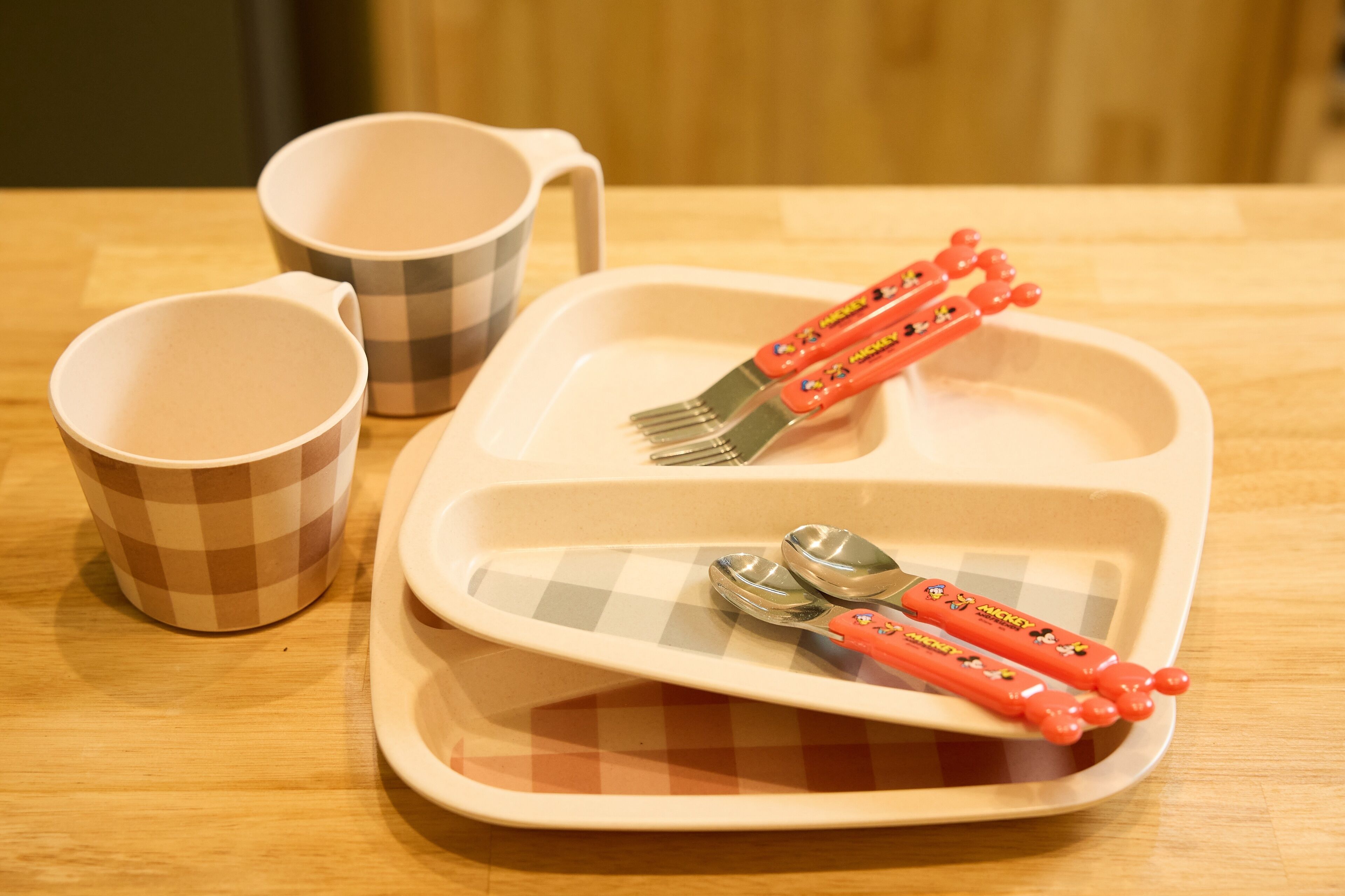 A table with a checkered tray, two cups, and two forks with Mickey Mouse designs.
