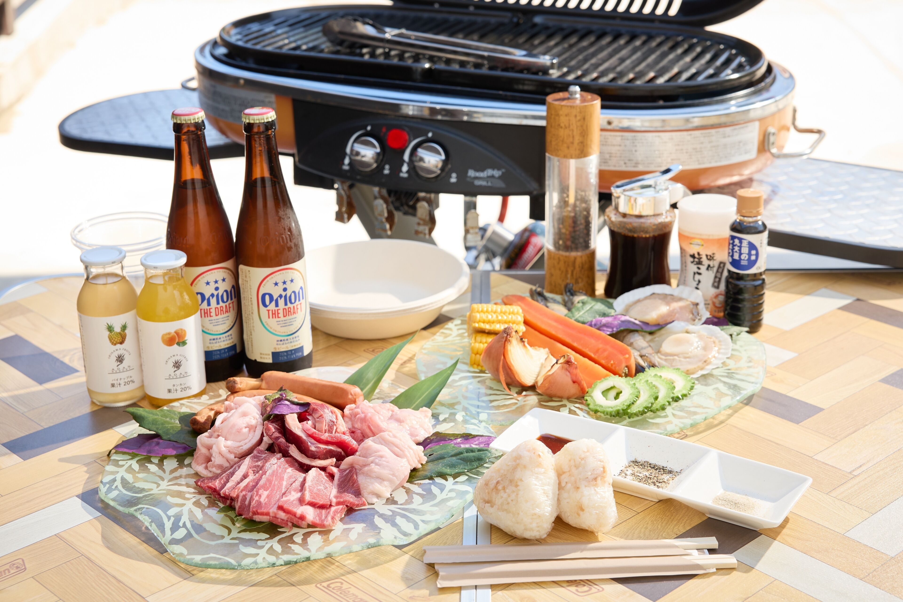 A table set with various food items, bottles of beer, and a grill in the background.