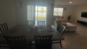 Un espace repas comprenant une table et des chaises, un canapé, un téléviseur et une vue sur une étendue d’eau par la fenêtre.