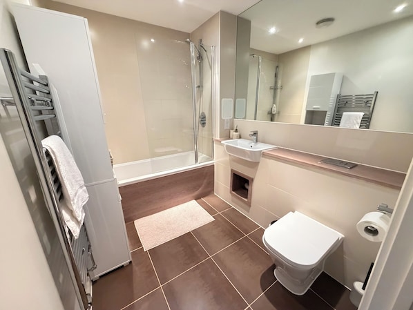 Un bany modern amb dutxa d'estuc de vidre, un lavabo blanc i un vàter.