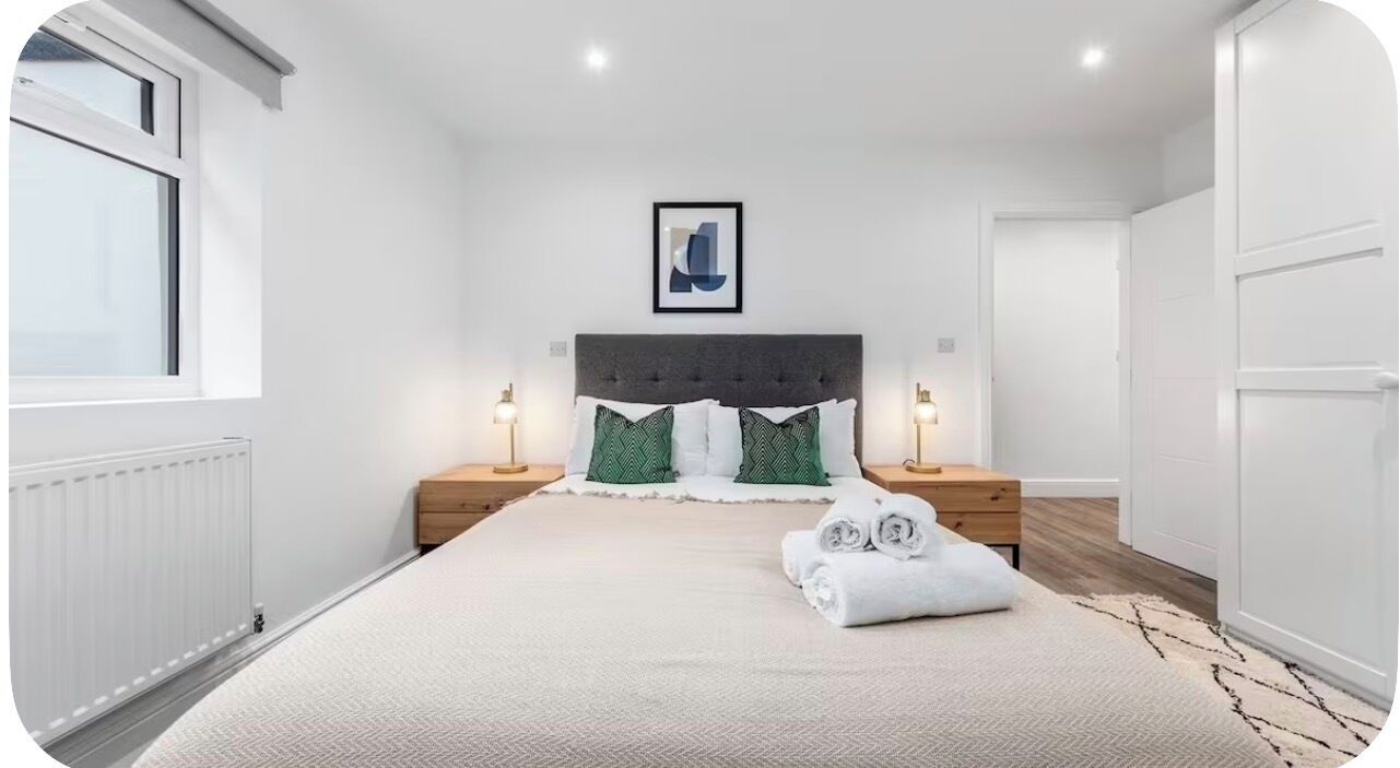 A bedroom with a bed, two bedside tables, a framed picture on the wall, and a window.