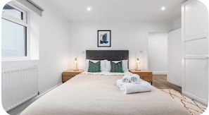 A bedroom with a bed, two bedside tables, a framed picture on the wall, and a window. - Luxury 2 Bedroom Duplex near O2 Arena, ExCeL Centre & Canary Wharf (London)