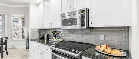 Una cocina moderna con armarios blancos, un microondas de acero inoxidable, una estufa negra y un plato de desayuno con croissants.