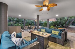 Un patio esterno con mobili in vimini, un tavolo con piano in vetro e una ventola a soffitto.