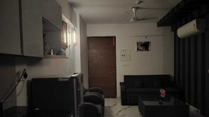 Een compacte woonruimte met een kitchenette, een bank, een bijzettafeltje en een plafondventilator.