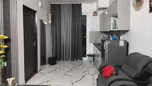 Een moderne woonkamer met een zwarte bank, een glazen salontafel en een rode sportbal. In de achtergrond is een keuken met een koelkast en een spoelbak zichtbaar.