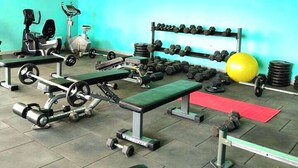 Een sportschool met trainingsapparatuur, een bank, gewichten en een gele fitnessbal.