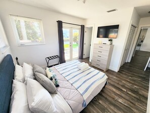 Ein Schlafzimmer mit einem Bett, einer Kommode, einem Fernseher und Blick ins Freie.