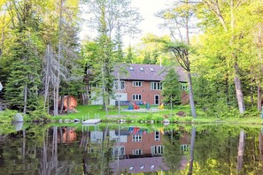 Une maison avec un quai s’avançant dans un lac paisible, entourée d’une forêt dense.