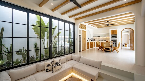 A modern living room with a large window, a sofa, and a dining area with wooden furniture. - Palmera Aalto Bingin (Pecatu)