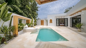 A modern outdoor pool area with a wooden pergola, surrounded by lush greenery and white walls. - Palmera Aalto Bingin (Pecatu)