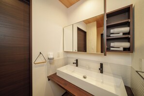 A modern bathroom with a large white sink, dark wooden countertop, and a mirror above the sink. - Lily House (Beppu)