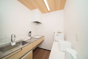 A modern kitchen with a stainless steel sink, white cabinets, a wooden ceiling, and a white countertop. - Lily House (Beppu)
