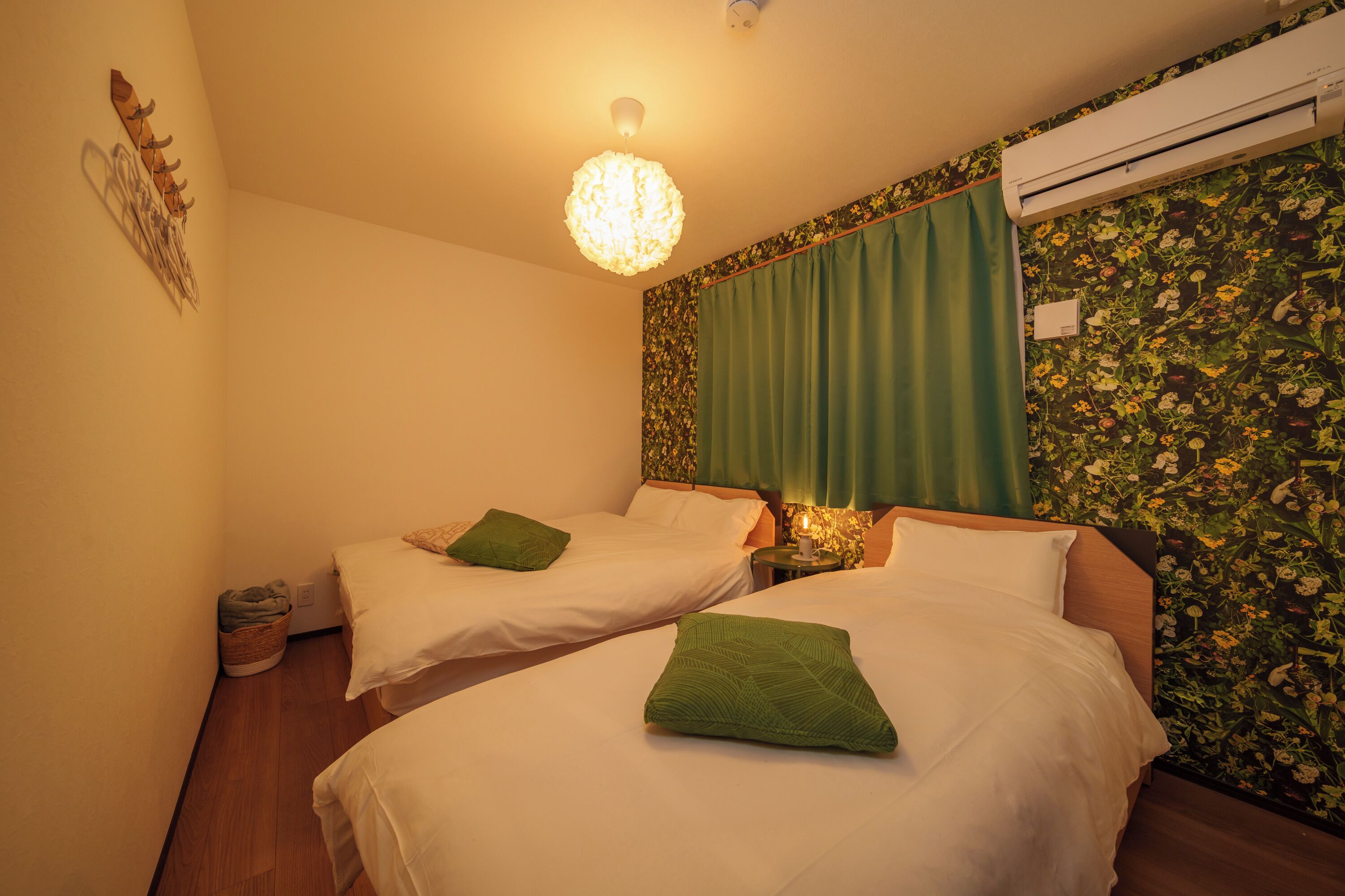 A hotel room with two beds, a chandelier, an air conditioner, and a floral wallpaper.