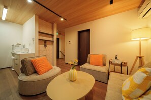 A modern living room with a round coffee table, two sofas with orange cushions, a small side table, and a lamp. - Lily House (Beppu)