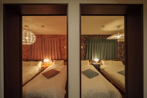 A mirrored room with two beds, each with a bedside table and lamp, floral wallpaper, and a hanging light fixture. - Lily House (Beppu)