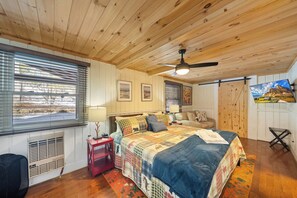 A cozy bedroom with a wooden ceiling, a large bed with a quilt, a red nightstand, a window with blinds, and a painting on the wall. - 3 BR Beech Mtn Basecamp: 2 Mi to Resort, Fireplace & Firepit (Beech Mountain)