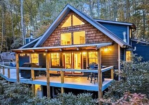 Une cabane en bois dotée d’une terrasse, de grandes fenêtres et d’une cheminée.